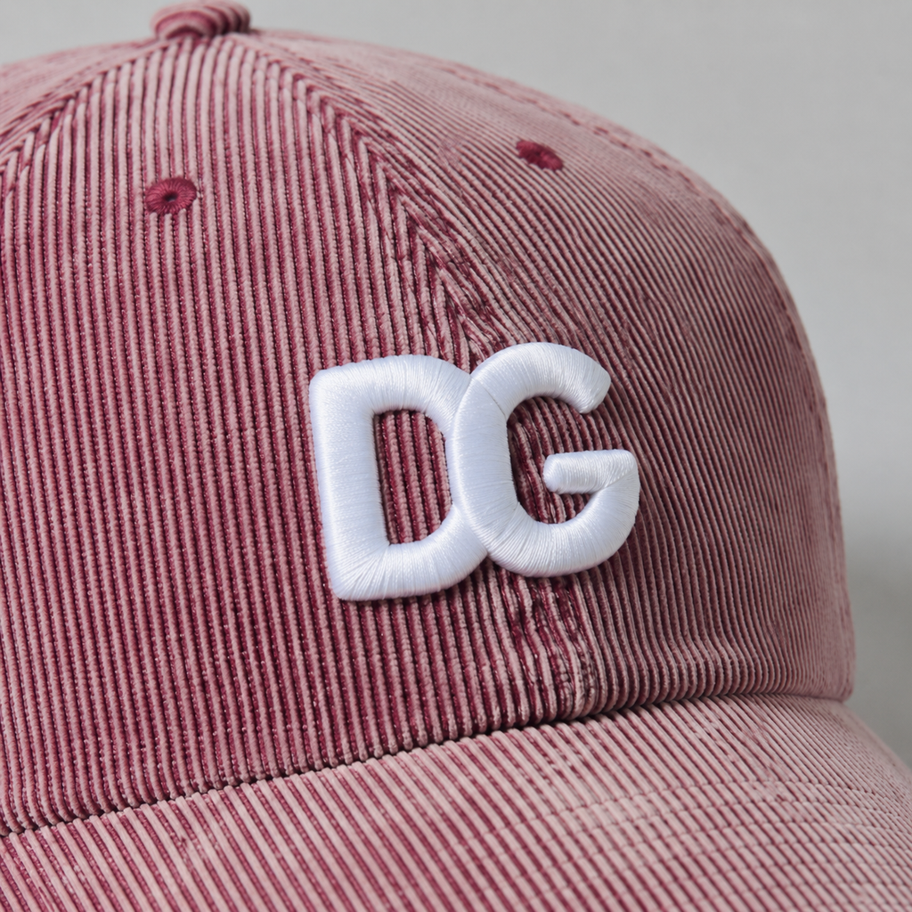 Close-up of raised white 3D embroidered DG logo on pink washed corduroy baseball cap.