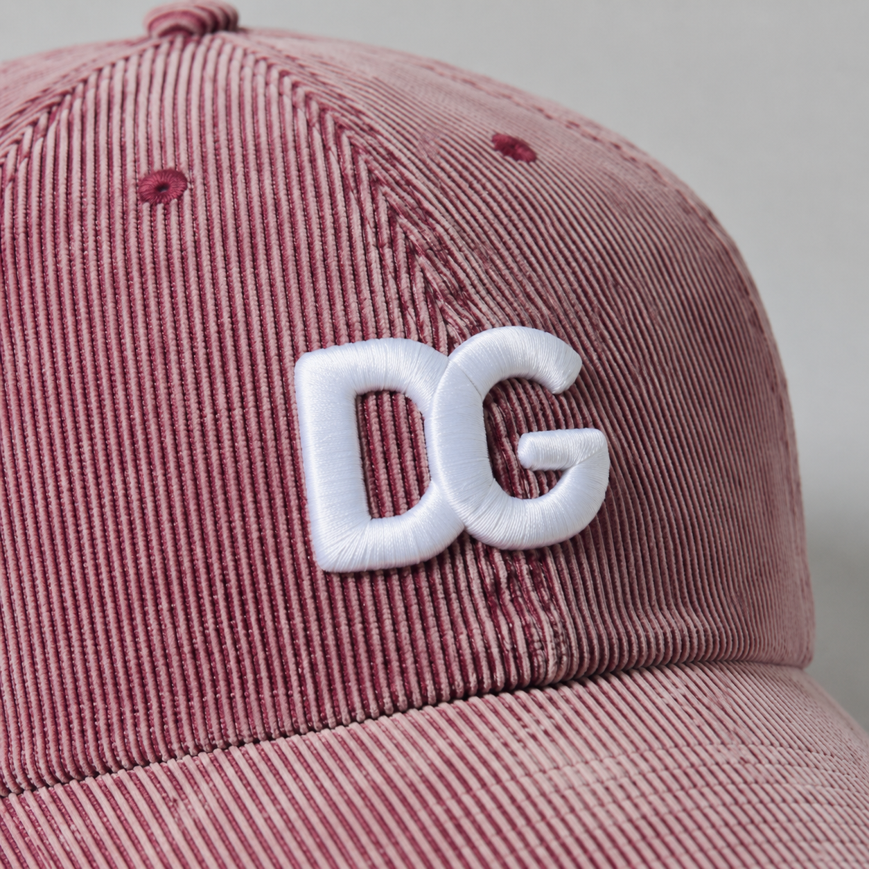 Close-up of raised white 3D embroidered DG logo on pink washed corduroy baseball cap.