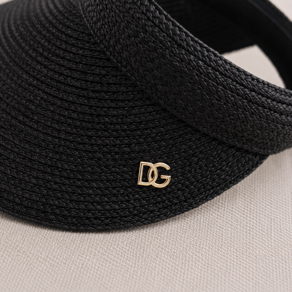 Close-up of black raffia sun visor with custom gold metal emblem logo and premium woven texture.
