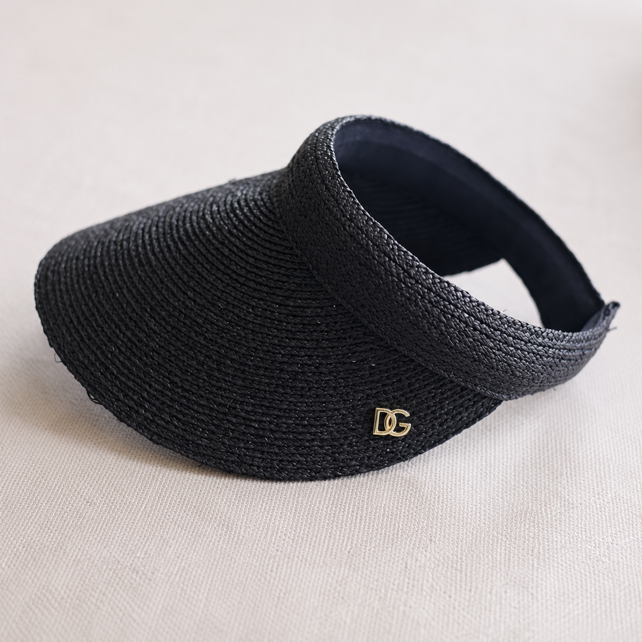 Side view of black raffia custom visor with curved brim, woven texture, and gold metal emblem logo.