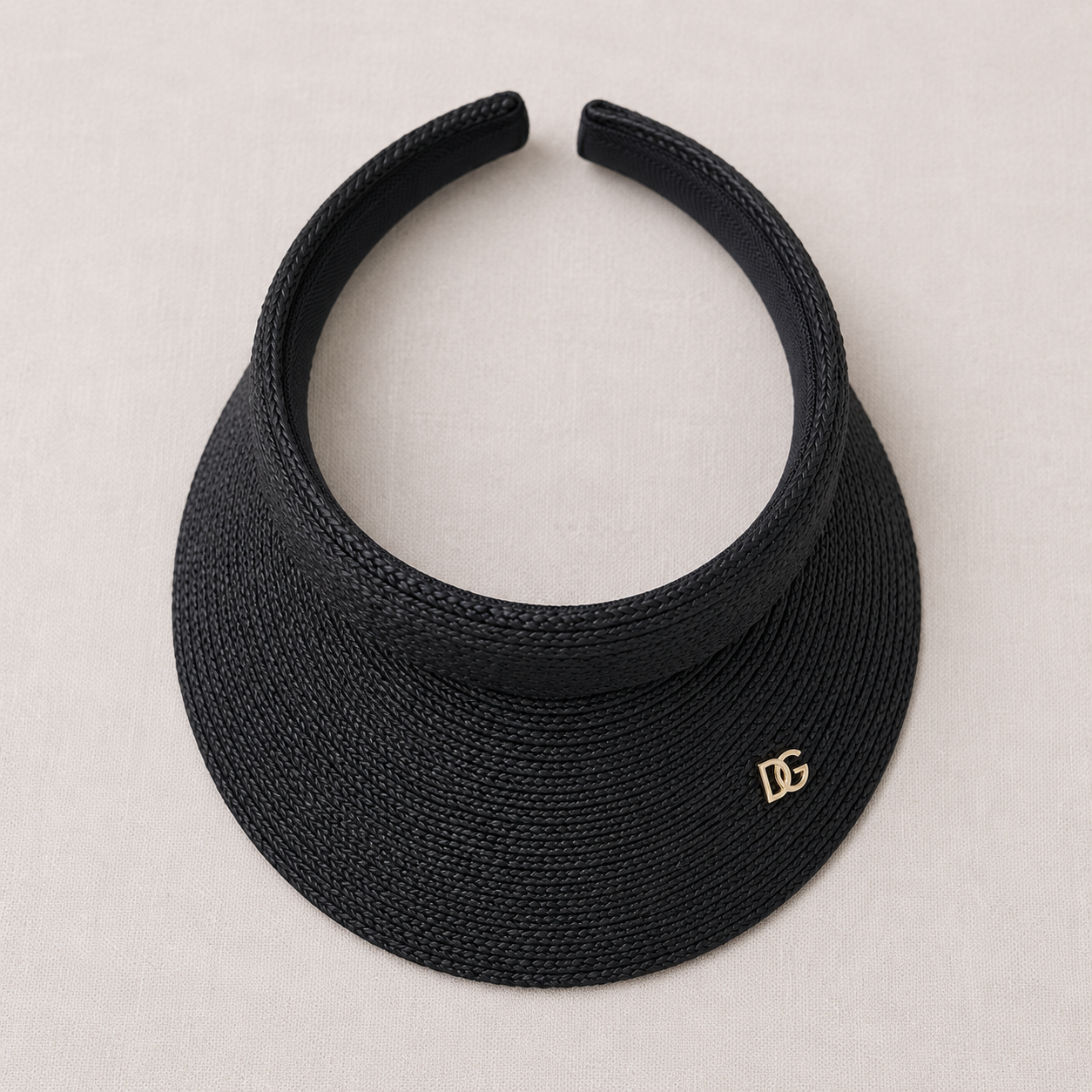 Top view of black raffia sun visor showing open-top structure, woven brim texture, and custom metal emblem detail.