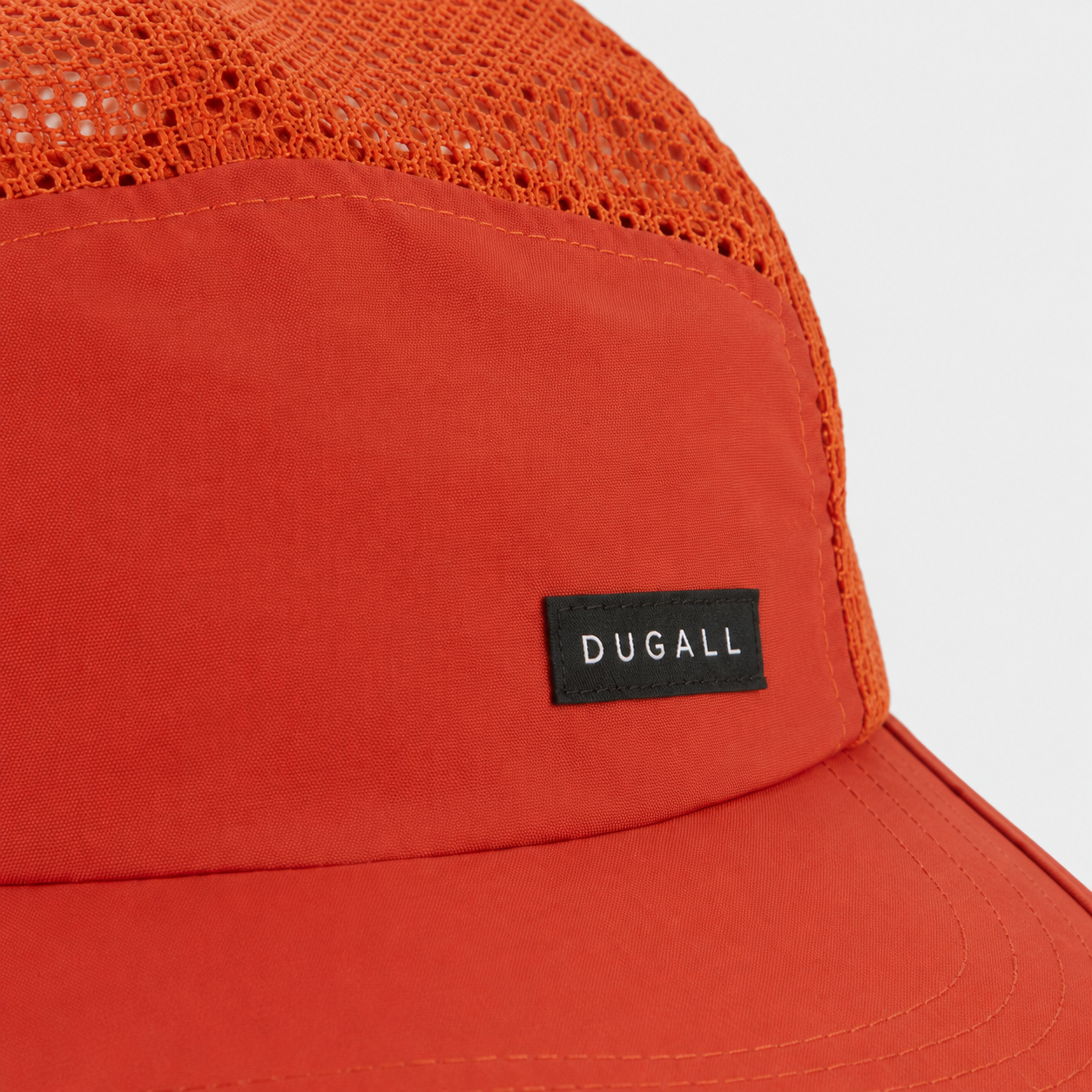 Close-up detail of the custom DUGALL label logo on an orange nylon 5 panel mesh cap