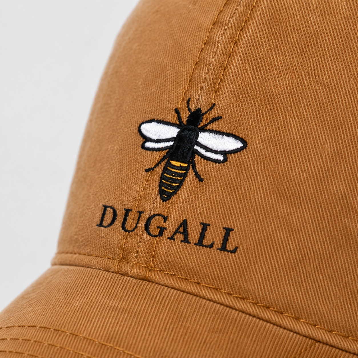 Close-up of bee embroidery logo on a honey brown washed cotton dad hat.