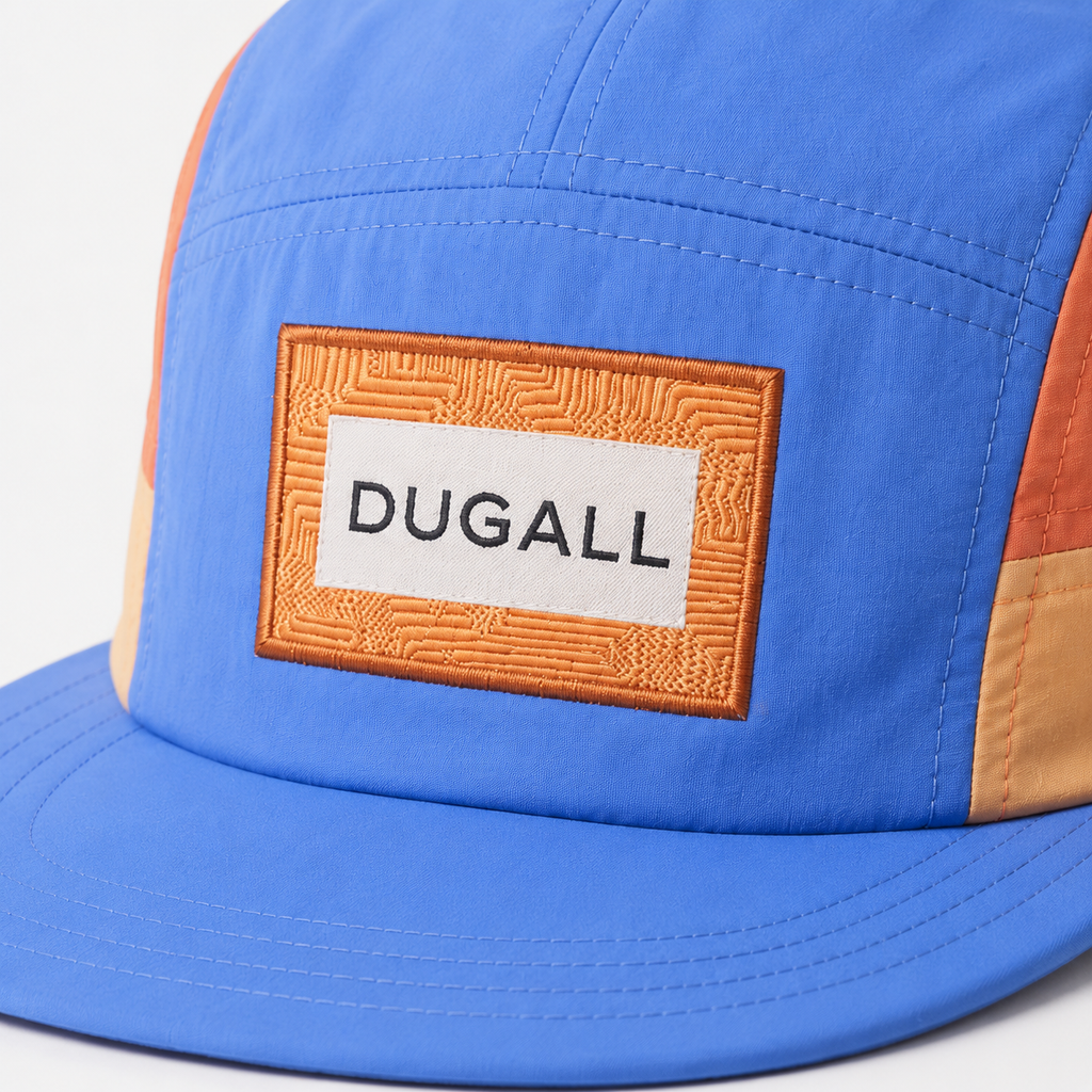 Close-up of custom patch label logo on a blue and orange color block nylon 5 panel baseball cap.