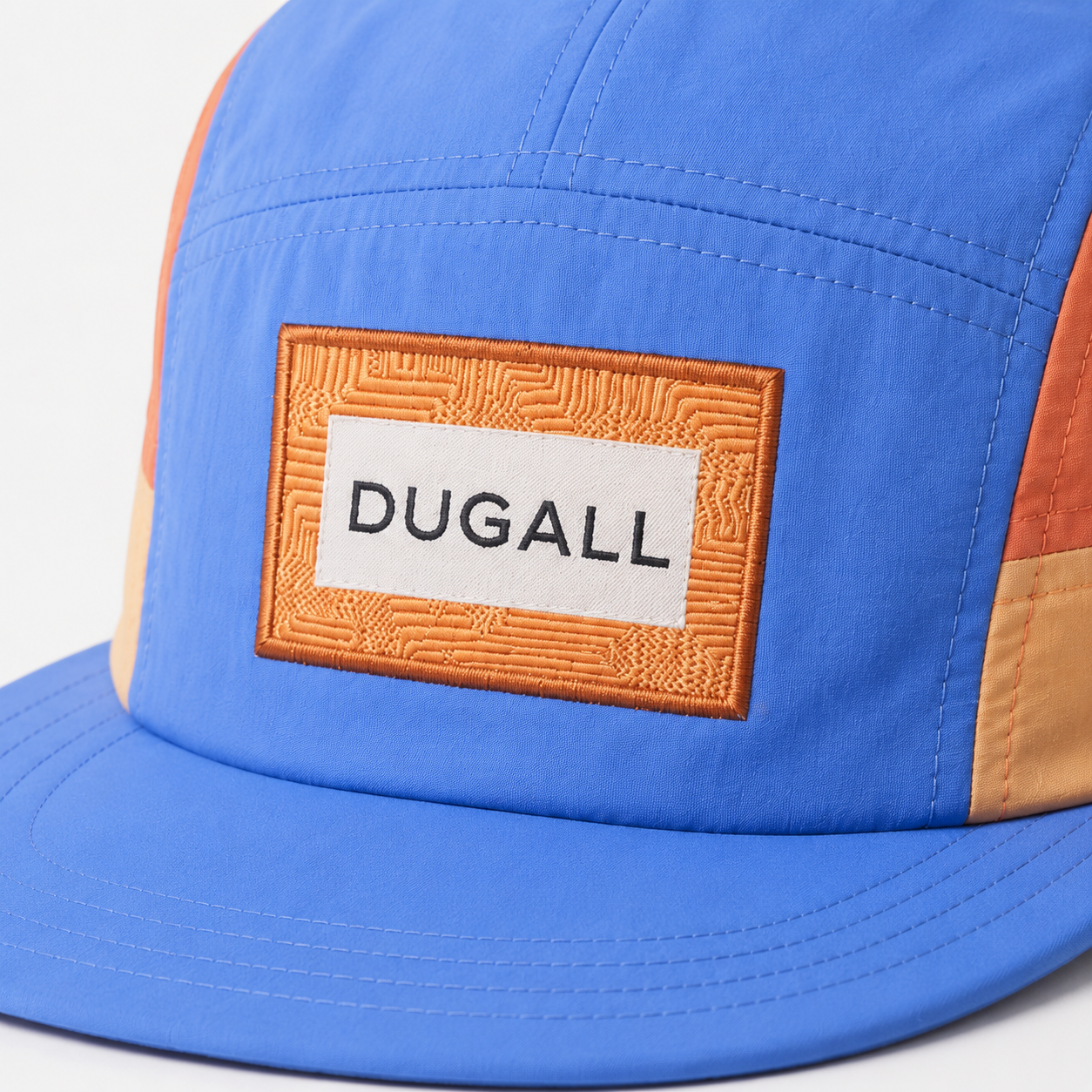 Close-up of custom patch label logo on a blue and orange color block nylon 5 panel baseball cap.