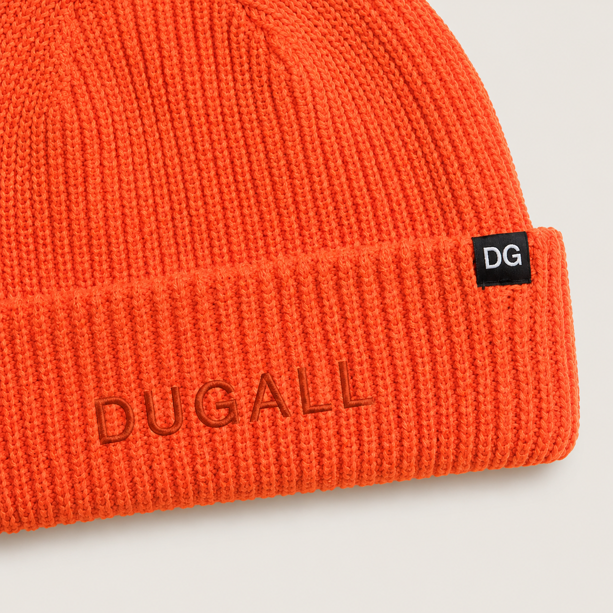 Close-up detail of the orange short knit beanie featuring tonal DUGALL embroidery and black DG side label branding