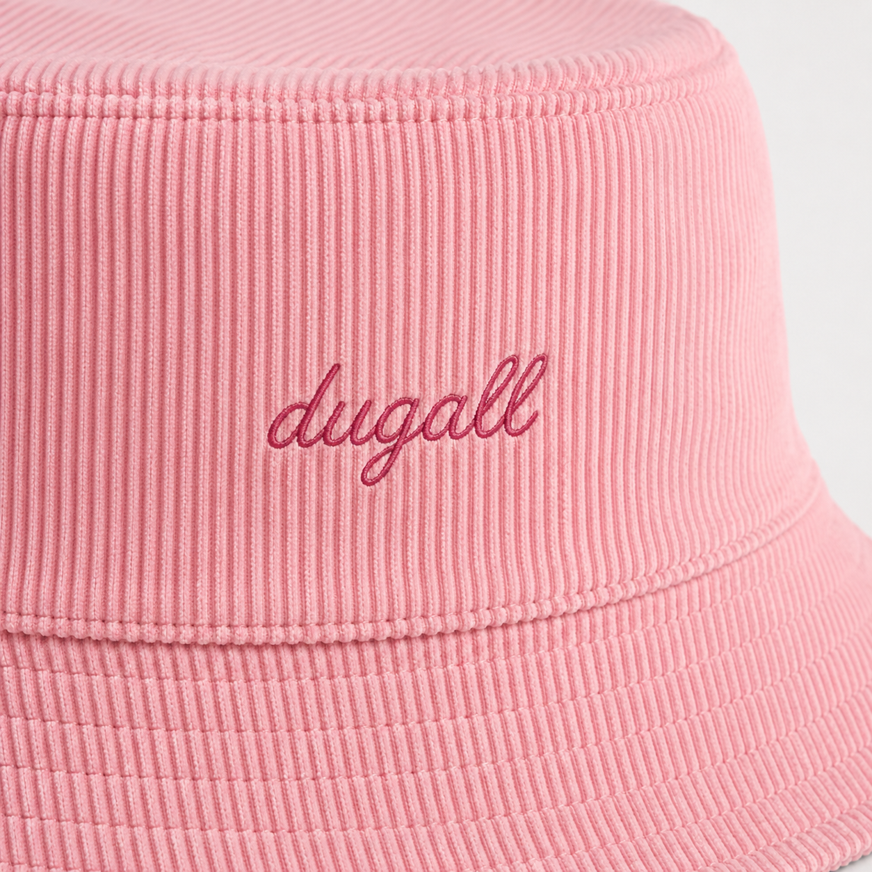 Close-up detail of embroidery logo on a pink cotton bucket hat with textured fabric.