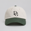 Front view of a custom dad hat with cream cotton crown, green faux suede brim, and black embroidered DG logo.