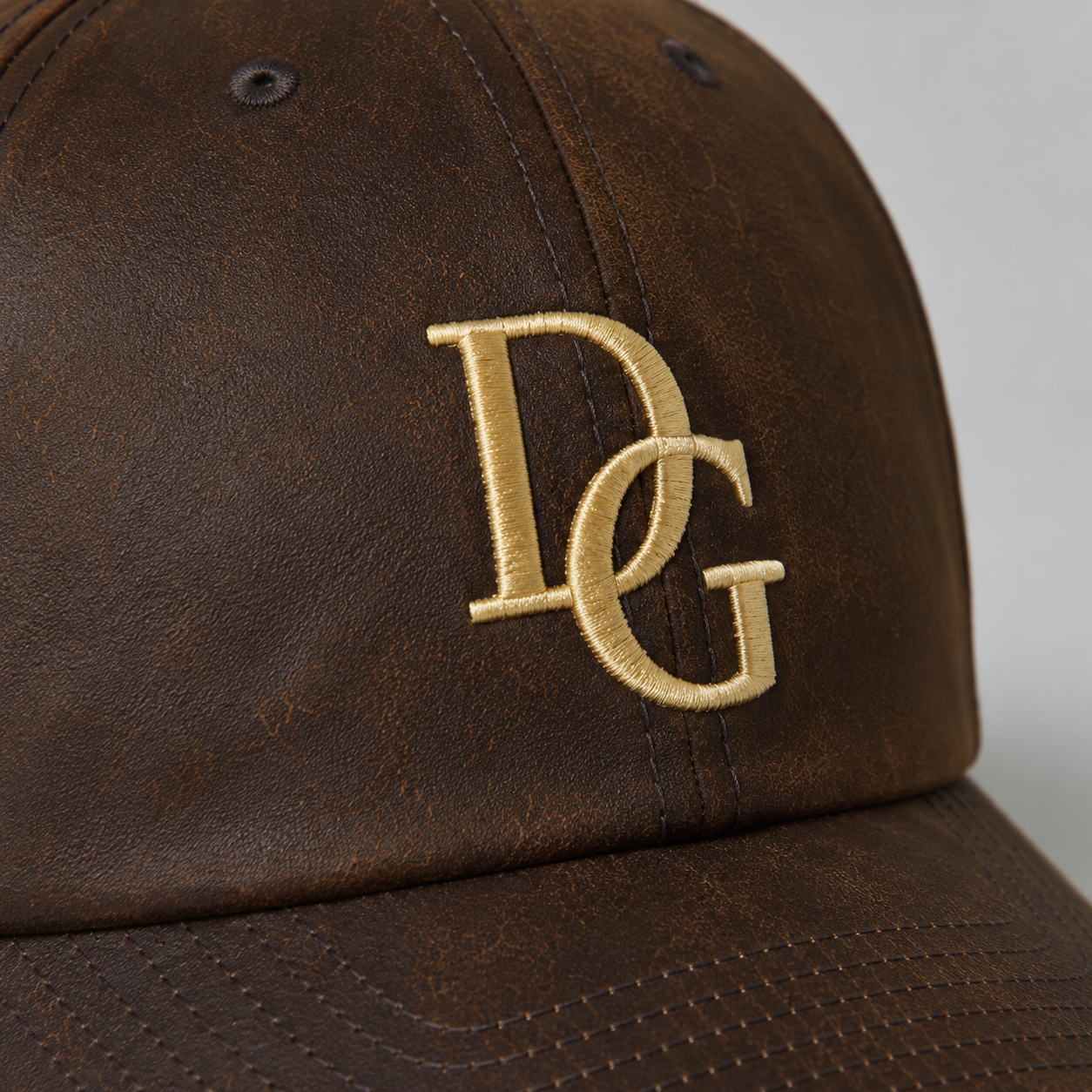 Close-up of gold custom embroidery logo on brown faux leather dad hat showing PU leather texture.