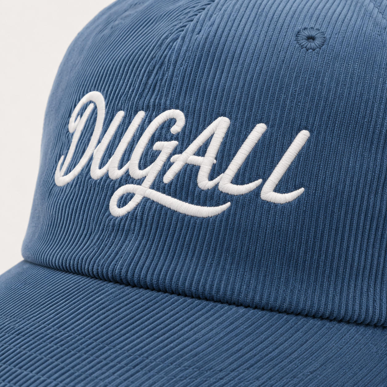 Close-up of white embroidered DUGALL logo on blue corduroy dad hat