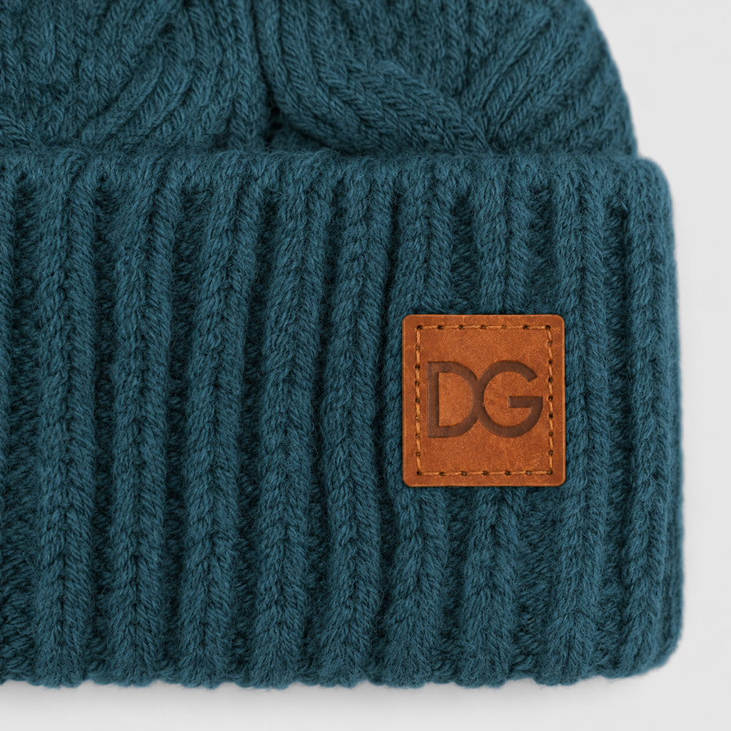Close-up of a custom leather patch logo on a teal cable knit pom pom beanie.