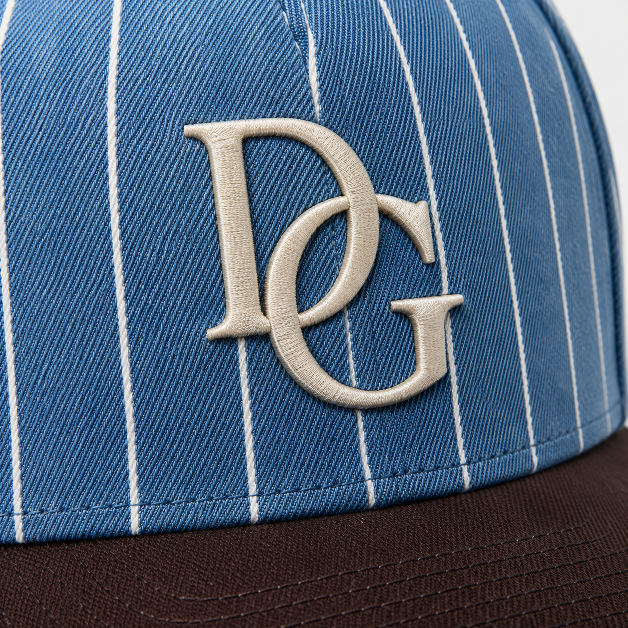 Close-up of raised custom embroidery logo on a blue pinstripe dad hat with brown curved brim.