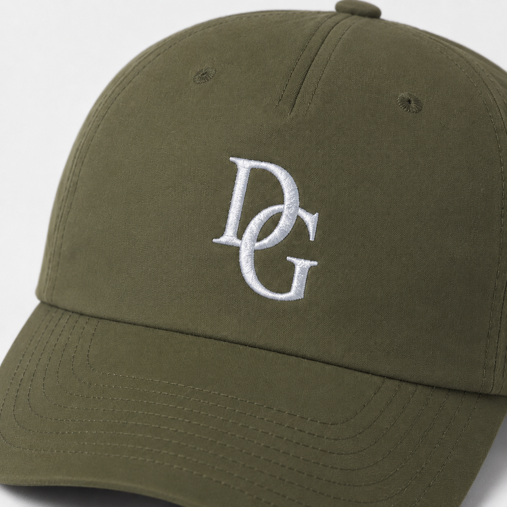 Close-up of white custom embroidered DG logo on olive green cotton twill baseball cap fabric.