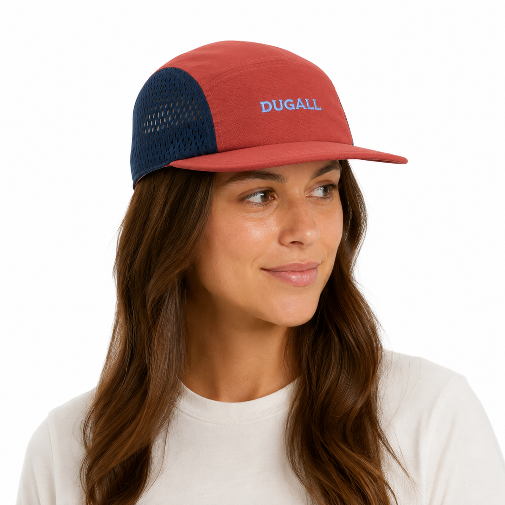 Female model wearing a custom color block mesh 5 panel cap with orange cotton front panel, navy mesh sides, and embroidered logo.
