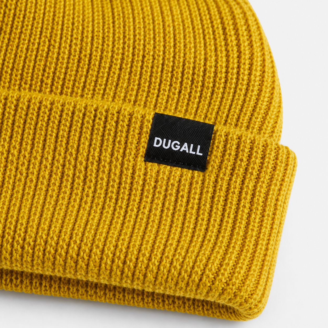 Close-up of custom woven label logo on a mustard yellow acrylic ribbed beanie.